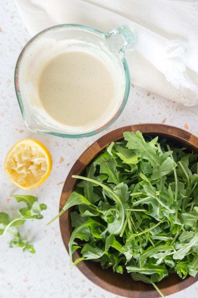 Bowl of arugula and measuring glass of dressing