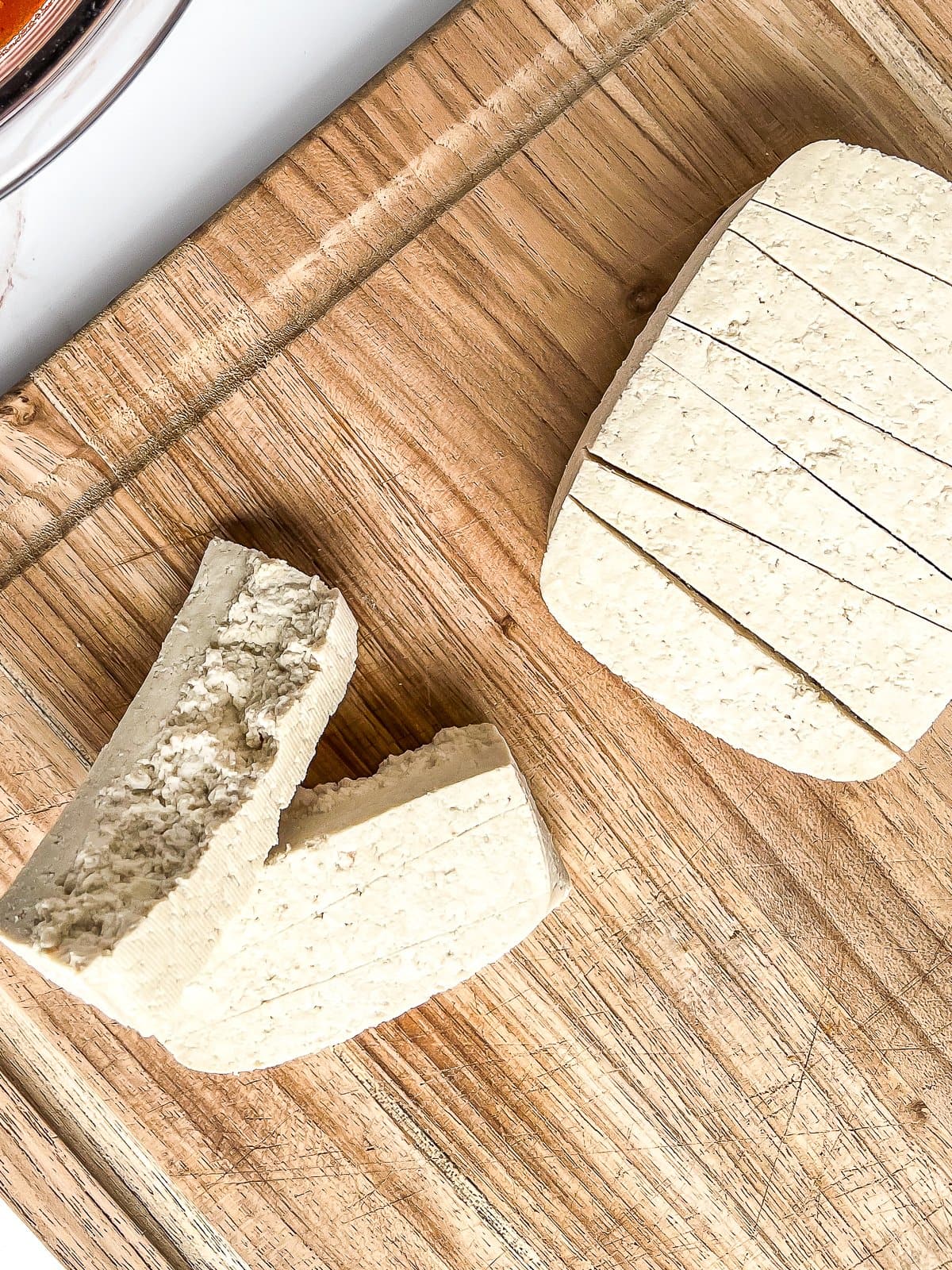 Close-up image of tofu scored into wedges and some tofu that has been ripped with irregular edges