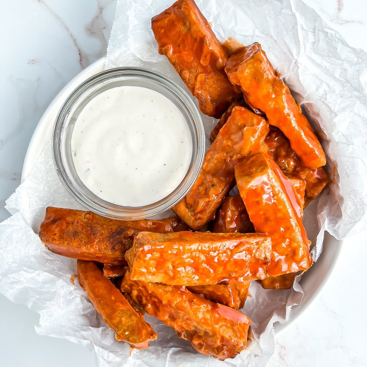plate of tofu wing glistening from buffalo sauce, with a cup of ranch for dipping