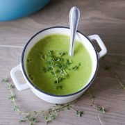 bowl of pale green pea soup topped with a few sprigs of fresh thyme