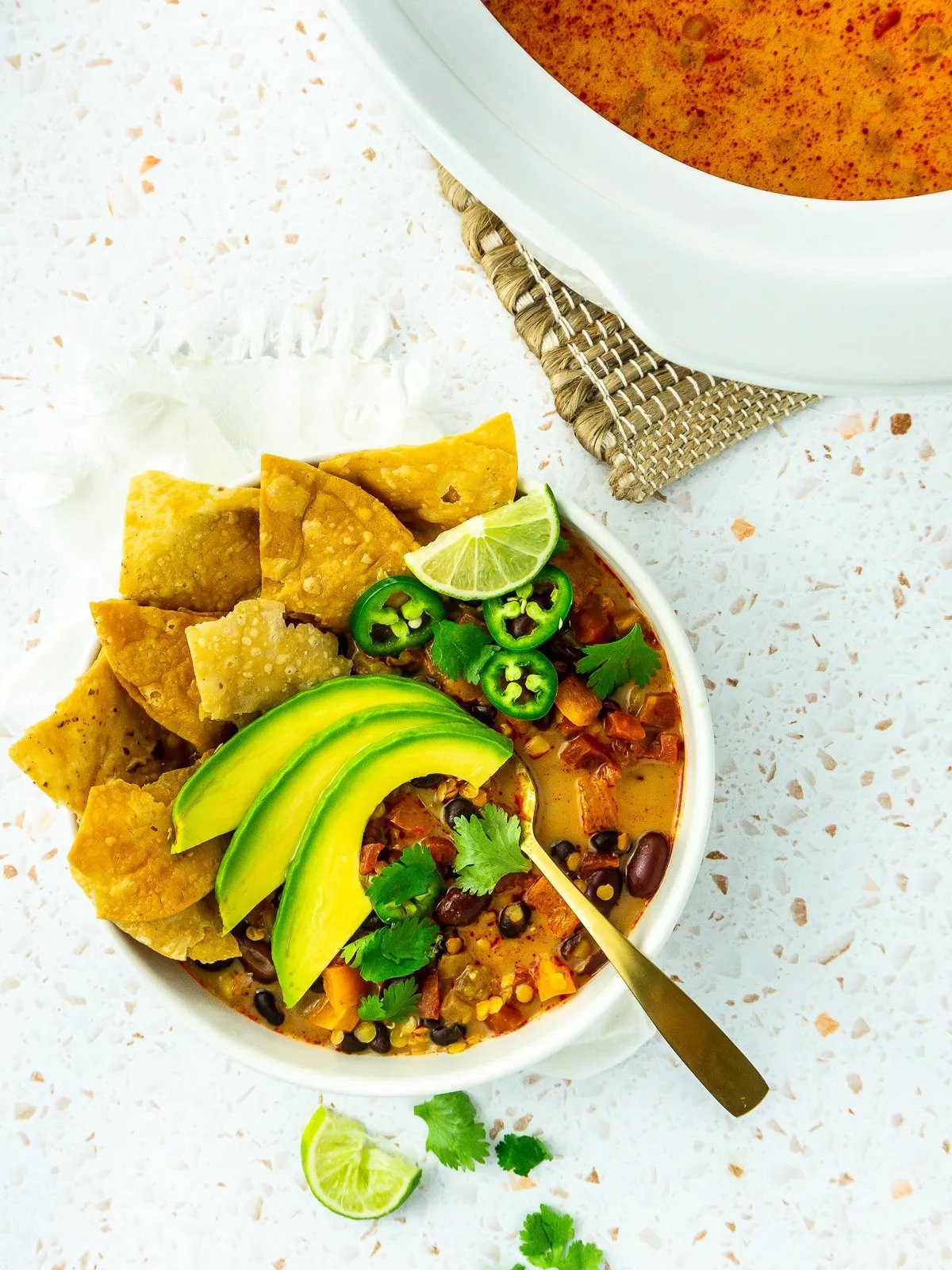 bowl of tortilla soup served from slow cooker and topped with avocado, tortilla chips, jalapeños, and lime wedges