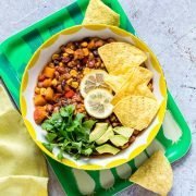 bowl of 3 bean chili topped with chips, avocado, cilantro, and slices of lemon