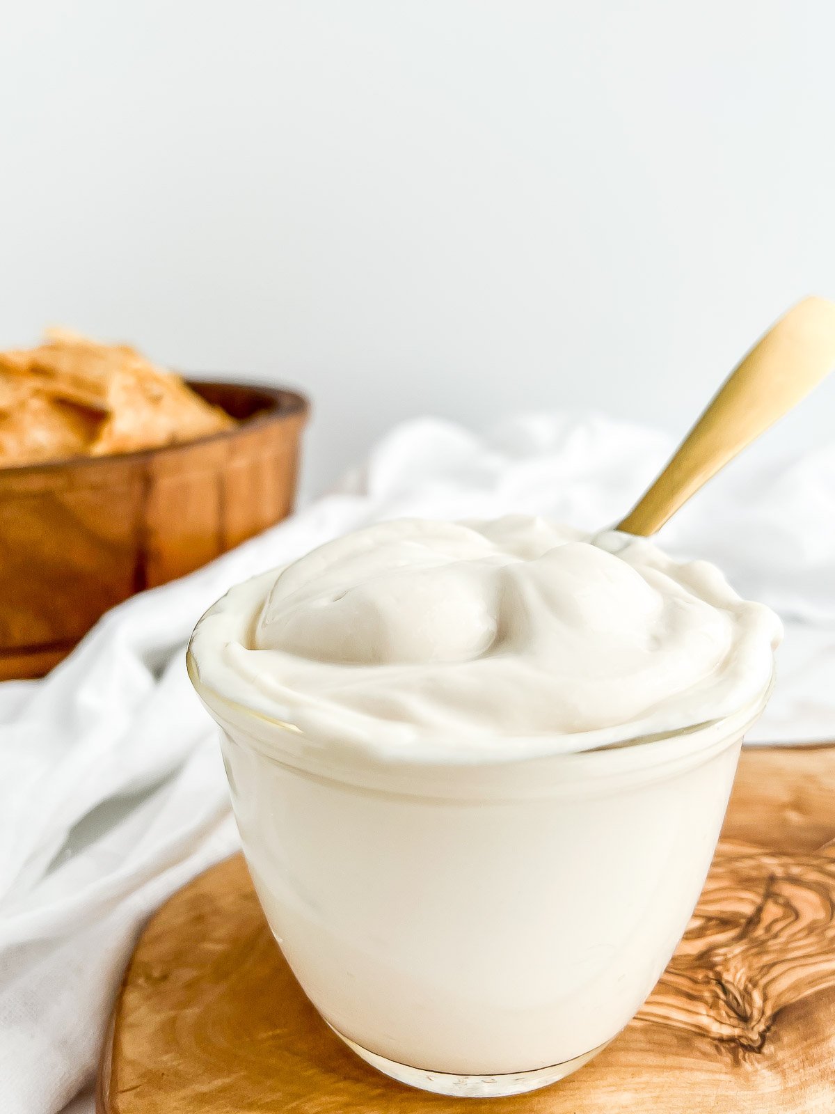 jar of sour cream with a spoon and bowl of chips in the background