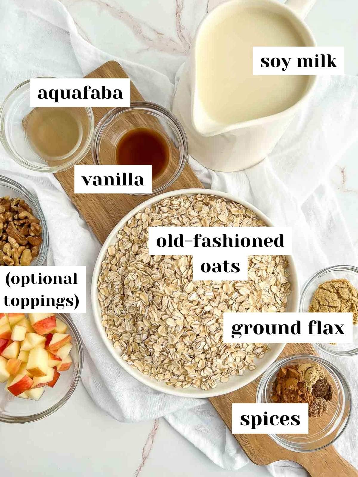 labeled ingredients including soy milk, oats, toppings, ground flaxseed, aquafaba, and spices on a white marble counter