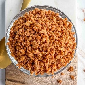 Close-up image of a bowl of vegan bacon bits on a stone and wood serving board with a gold spoon