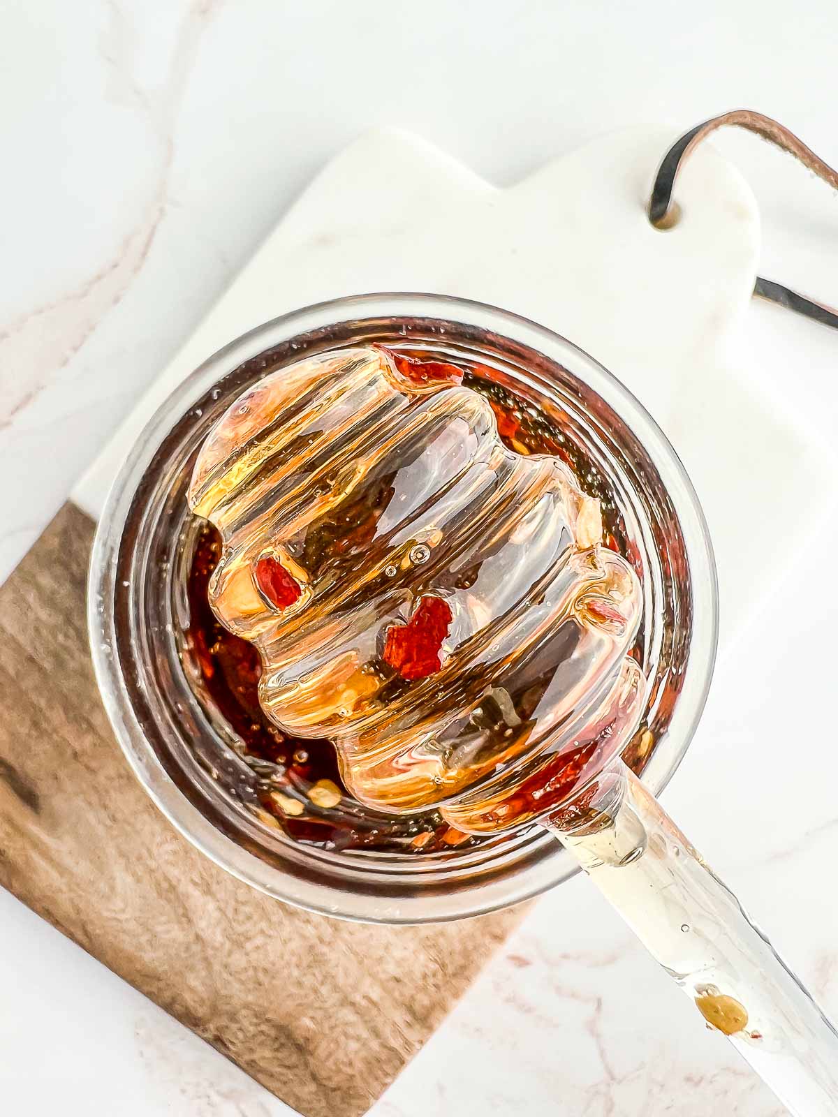 hot vegan honey on a honey dipper over a jar and a serving board.