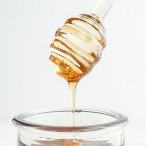 Vegan honey drizzling from a honey dipper into a jar.