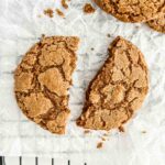 Close-up of gingersnap snapped in half on parchment paper.
