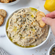 Hand dipping a cracker into a bowl of everything bagel hummus.