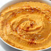 Swirled red pepper hummus topped with seasoning and sesame seeds.
