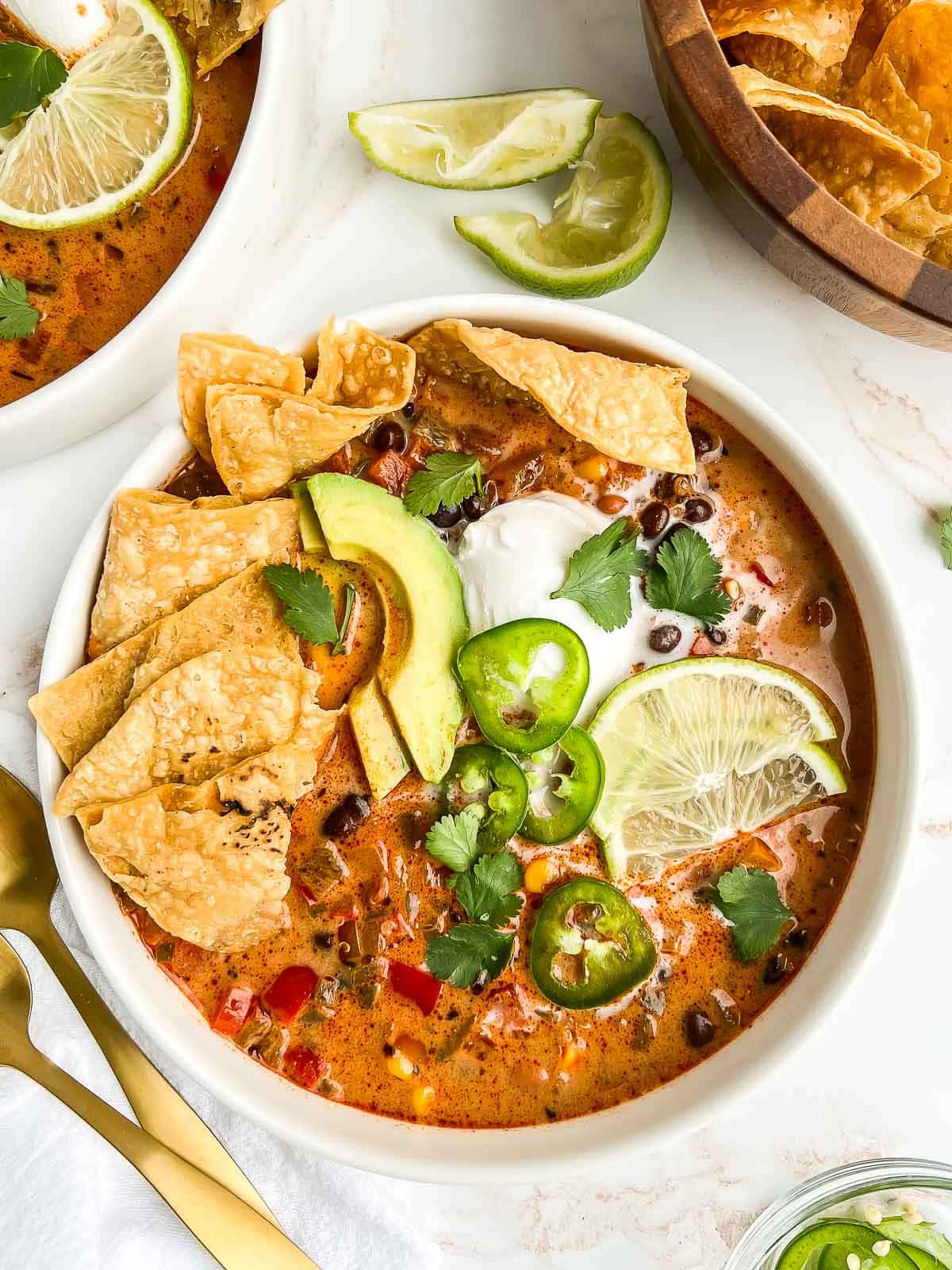Bowl of enchilada soup with toppings, another bowl of soup and bowl of tortilla chips nearby.