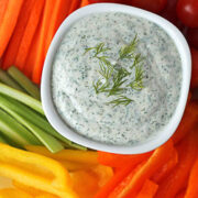 Bowl of veggie dip topped with dill surrounded by rainbow veggies.