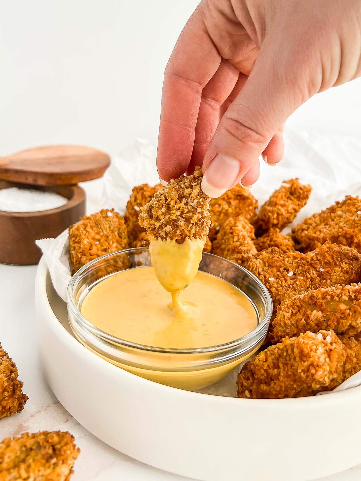 Hand dipping tofu nugget into chick-fil-a sauce.