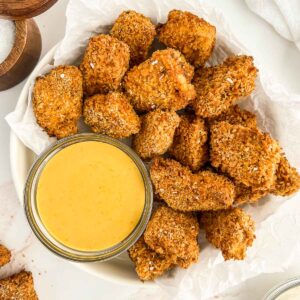 Bowl of tofu nuggets on parchment paper and dipping sauce.