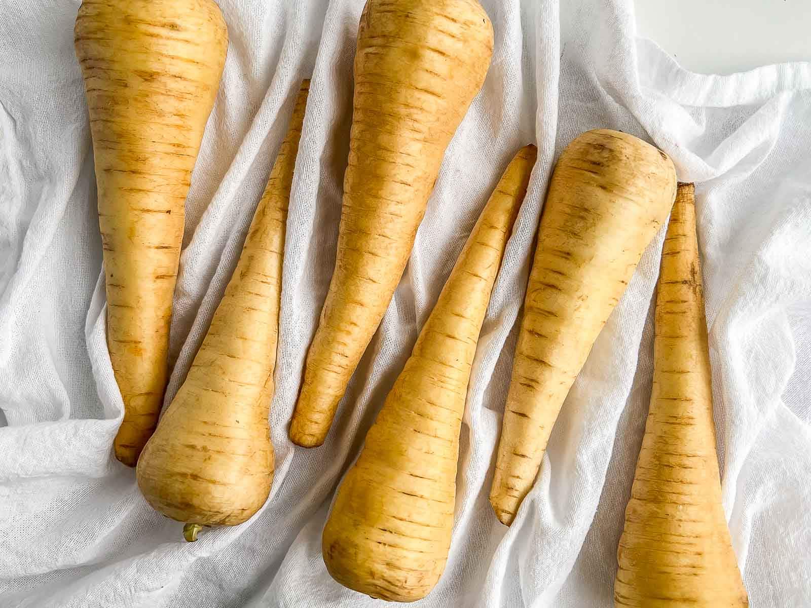 Several parsnips laid across a tea towel, opposite ends forming a zig-zag pattern.