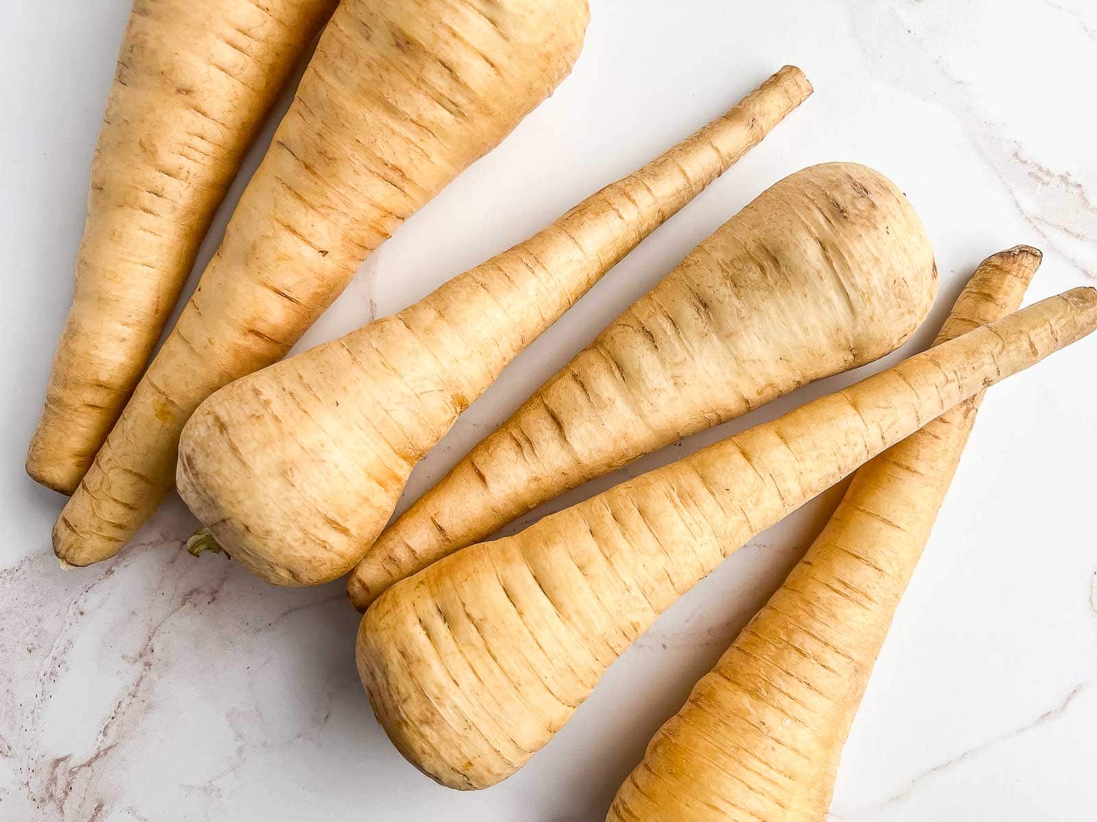 Whole parsnips laid across a marble counter.