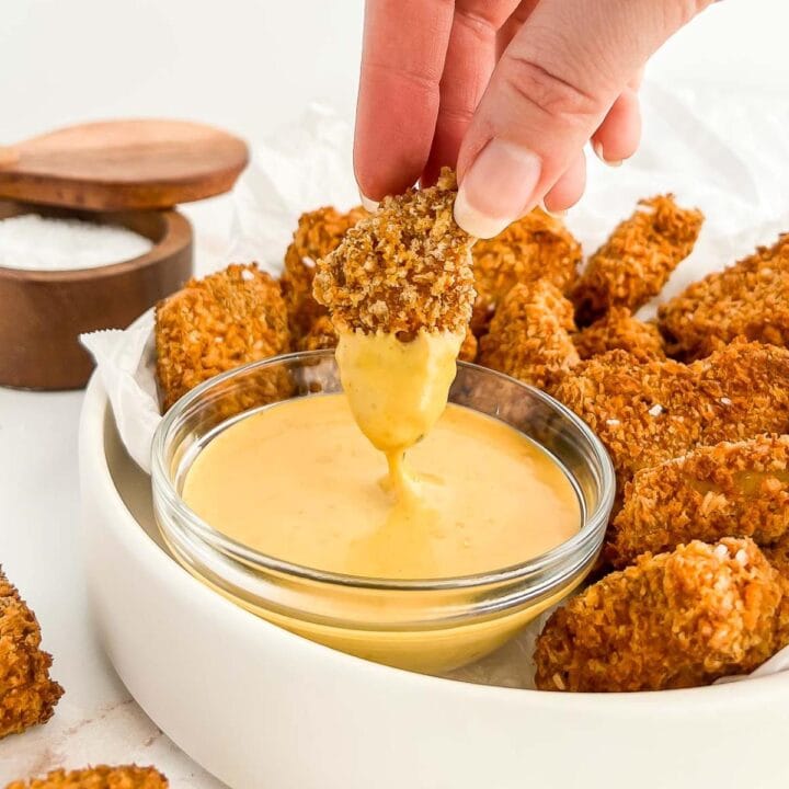 Hand dipping a tofu nugget into copycat chick-fil-a sauce.