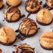 Coconut macaroon cookies on parchment paper with chocolate drizzled on top.