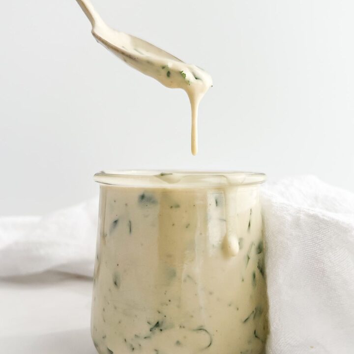 Tahini lime dressing being drizzled from a spoon into a jar.
