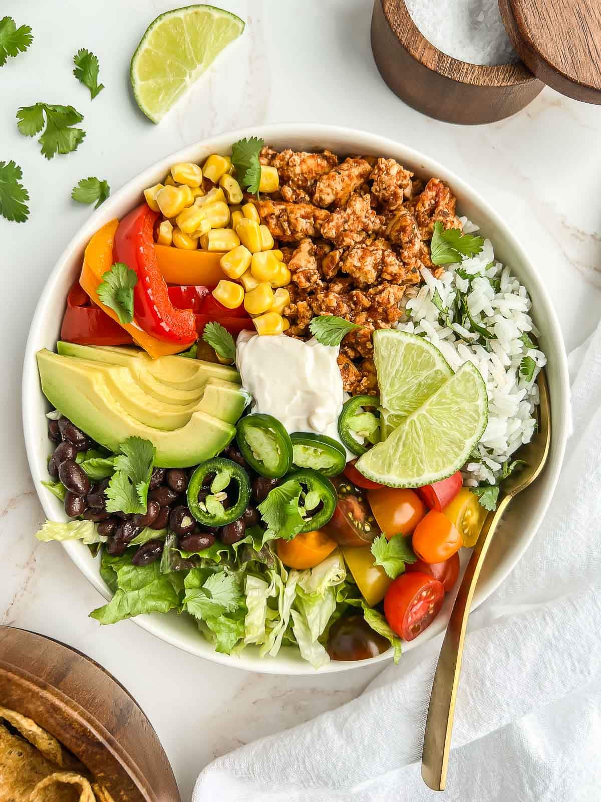 Tofu burrito bowl with a fork tucked in and cilantro and a lime wedge sprinkled about.