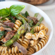 Close-up of a bowl of creamy chickpea pasta with asparagus and fresh basil.