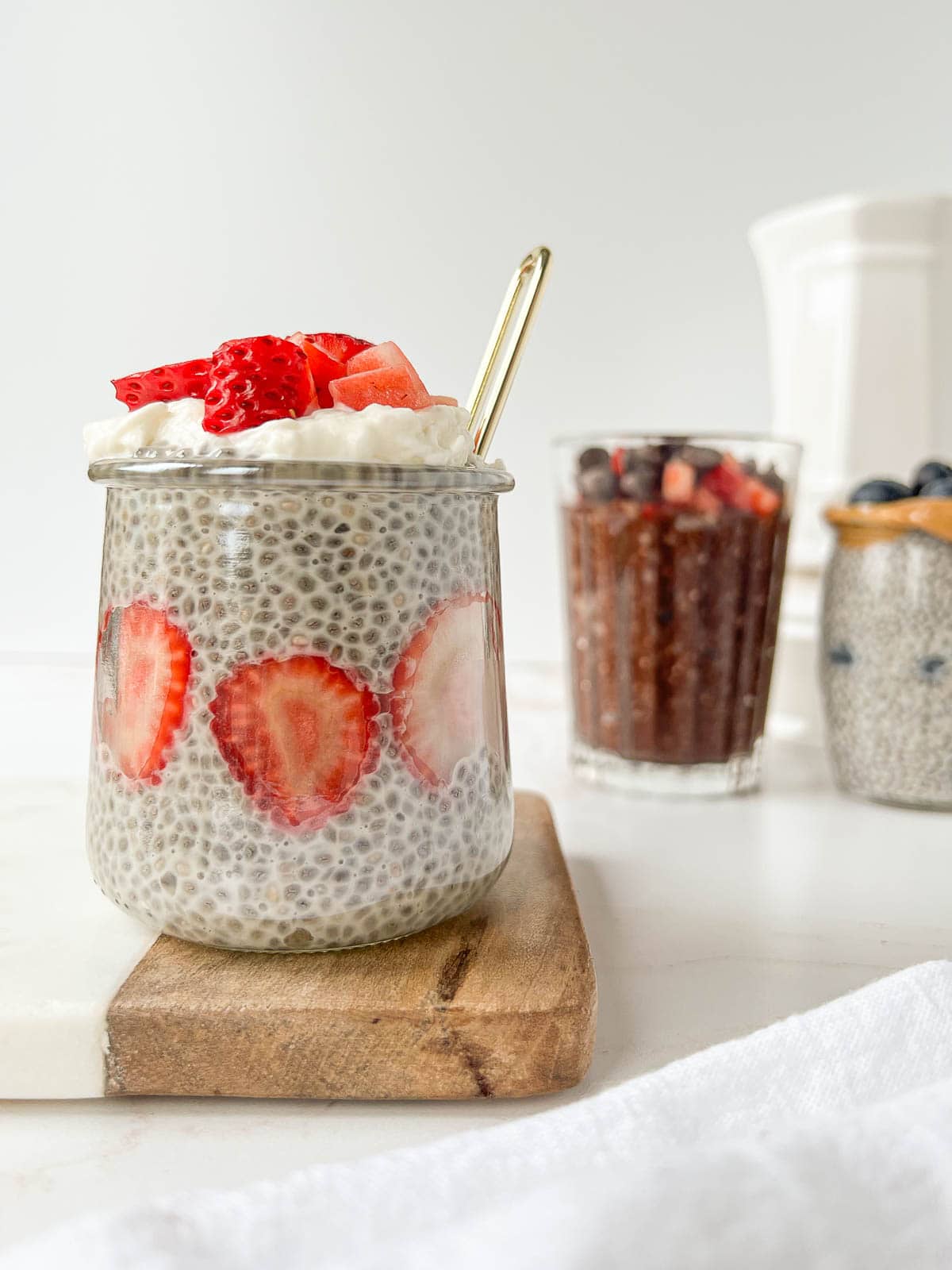 glass jar of chia pudding with fresh cut strawberries and coconut cream on a serving board.
