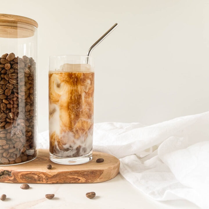 Cold brew latte on a wood board next to a jar of coffee beans.