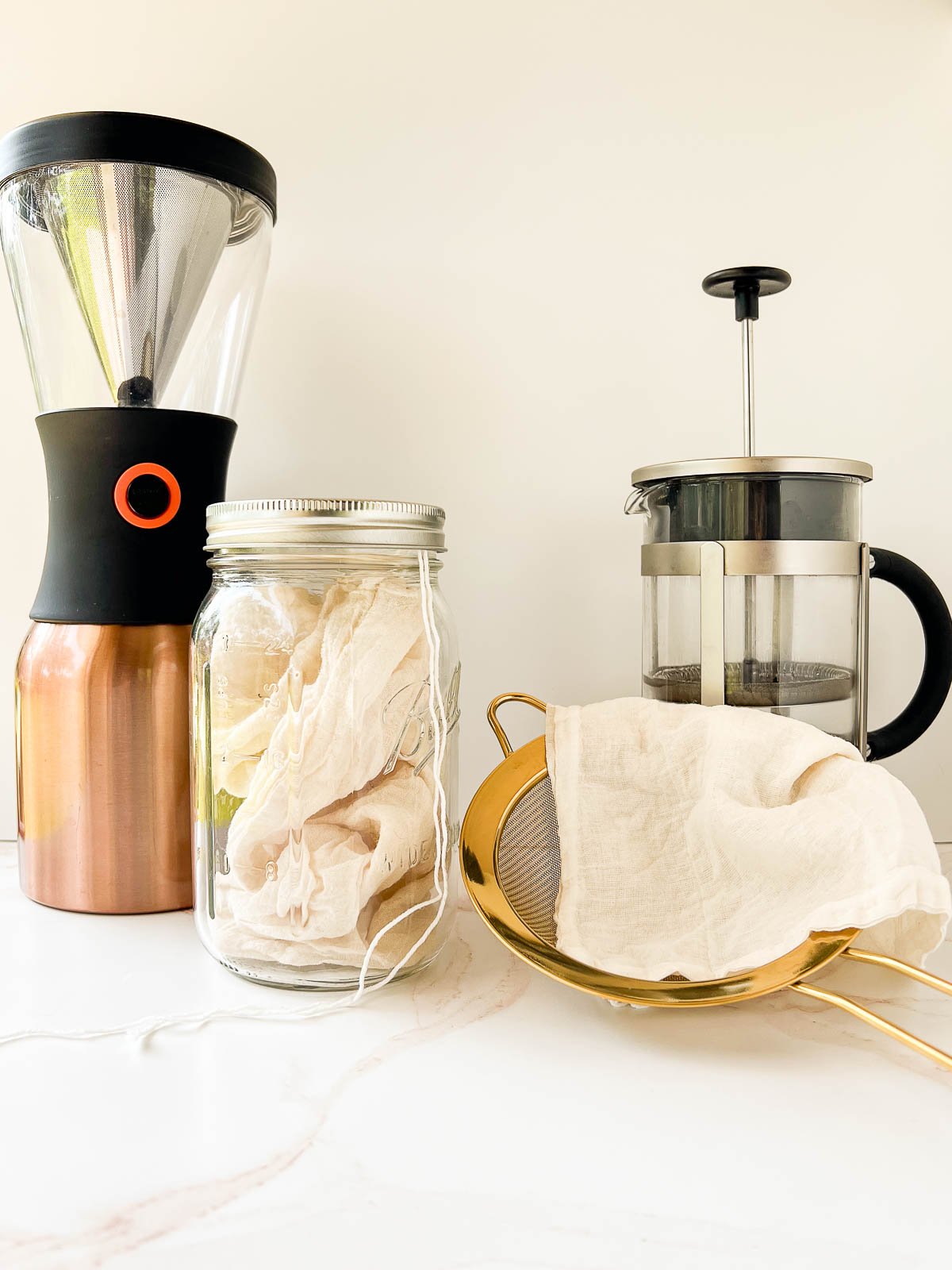 Different equipment including a cold brew maker, a jar and a cheesecloth bag, a french press, and a strainer lined with a cheesecloth.