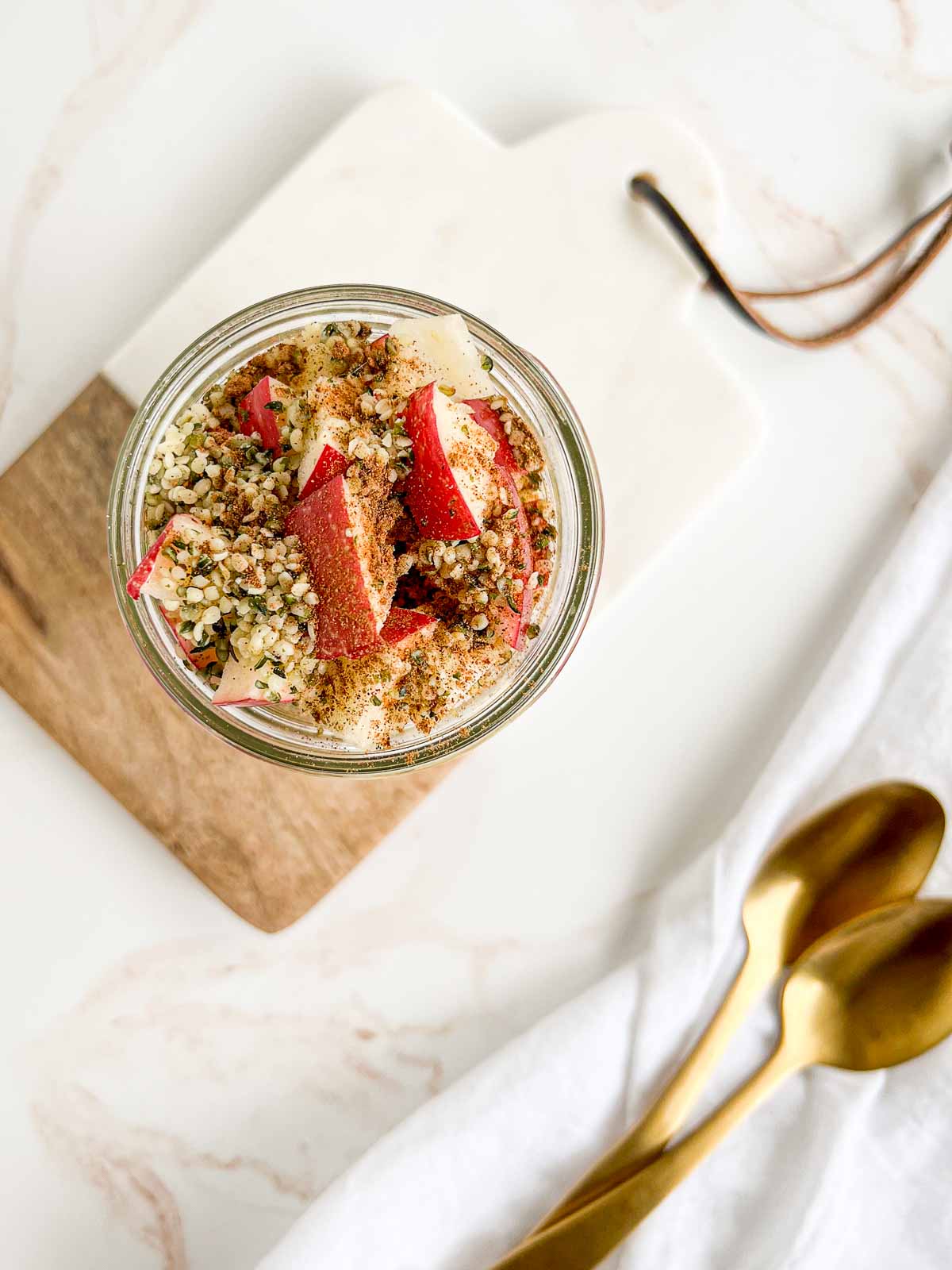 chia pudding topped with apples, hemp hearts, and cinnamon on a serving board with a couple of gold spoons.