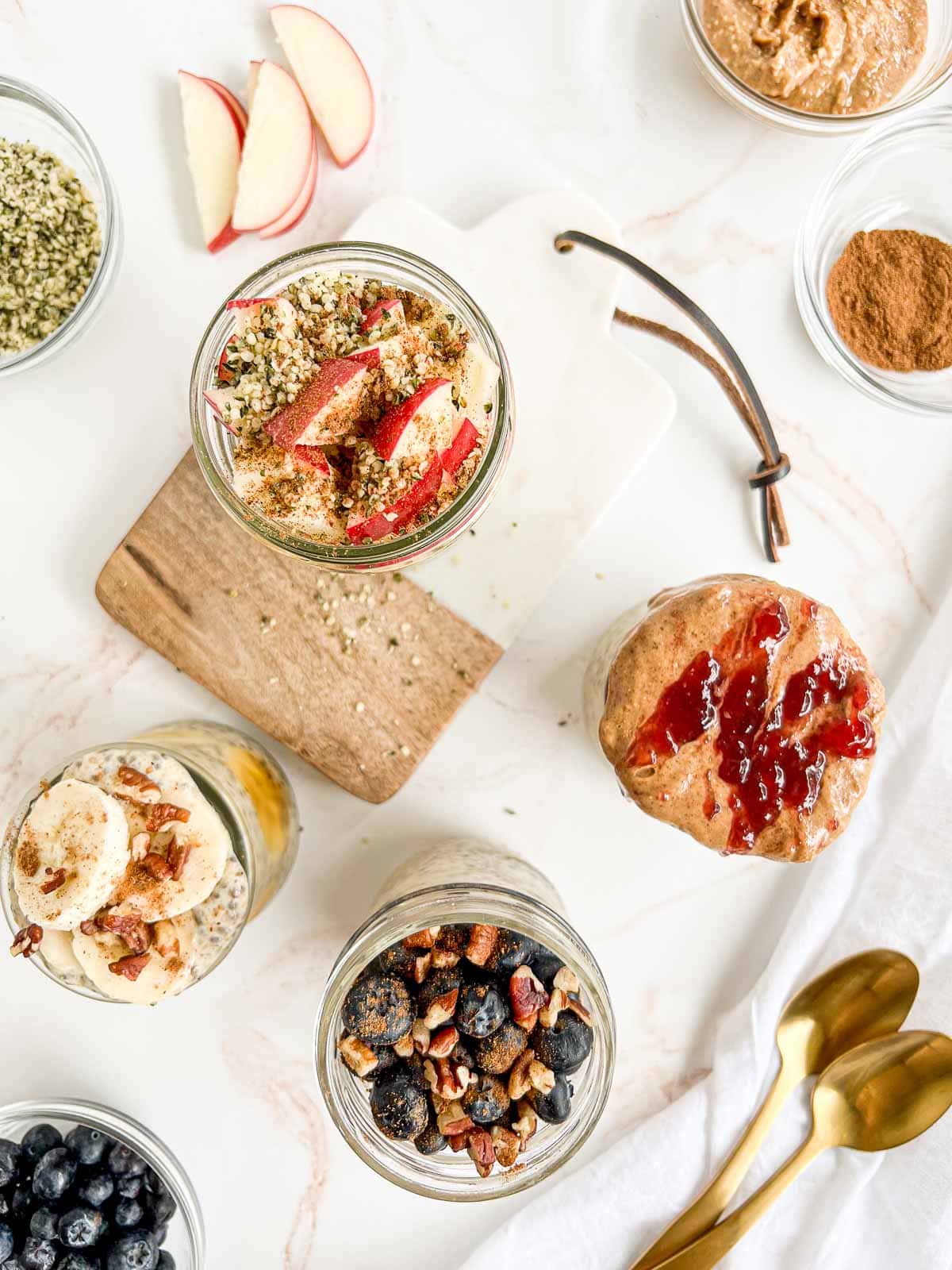 several jars of chia flax pudding with various toppings and some small bowls with topping ingredients nearby.