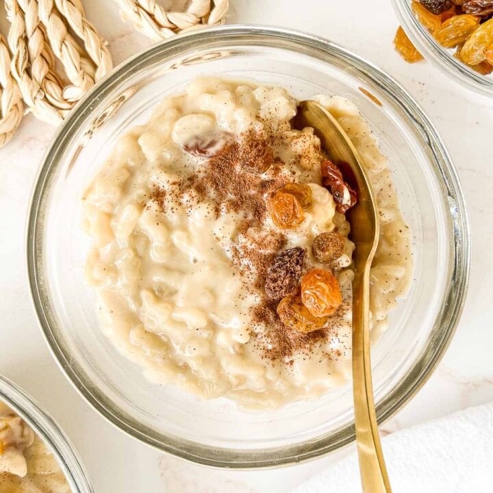 Bowl of warm rice pudding, topped with golden raisins and cinnamon with a spoon tucked in.