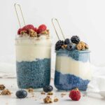 Two glass jars of blue chia pudding layered with vegan yogurt.
