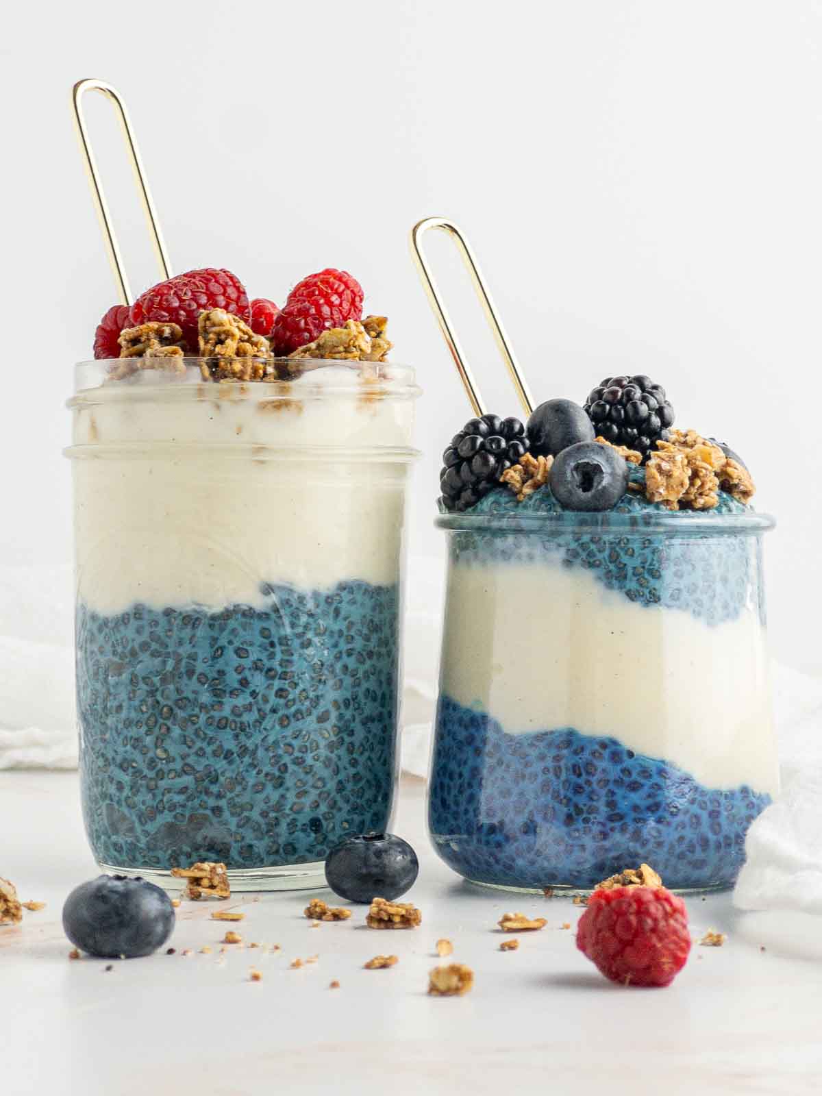 Two glass jars of blue chia pudding layered with vegan yogurt.